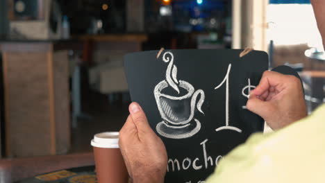 man writing coffee price on chalk board