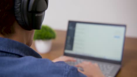chico poniéndose los auriculares y desplazándose en su computadora portátil