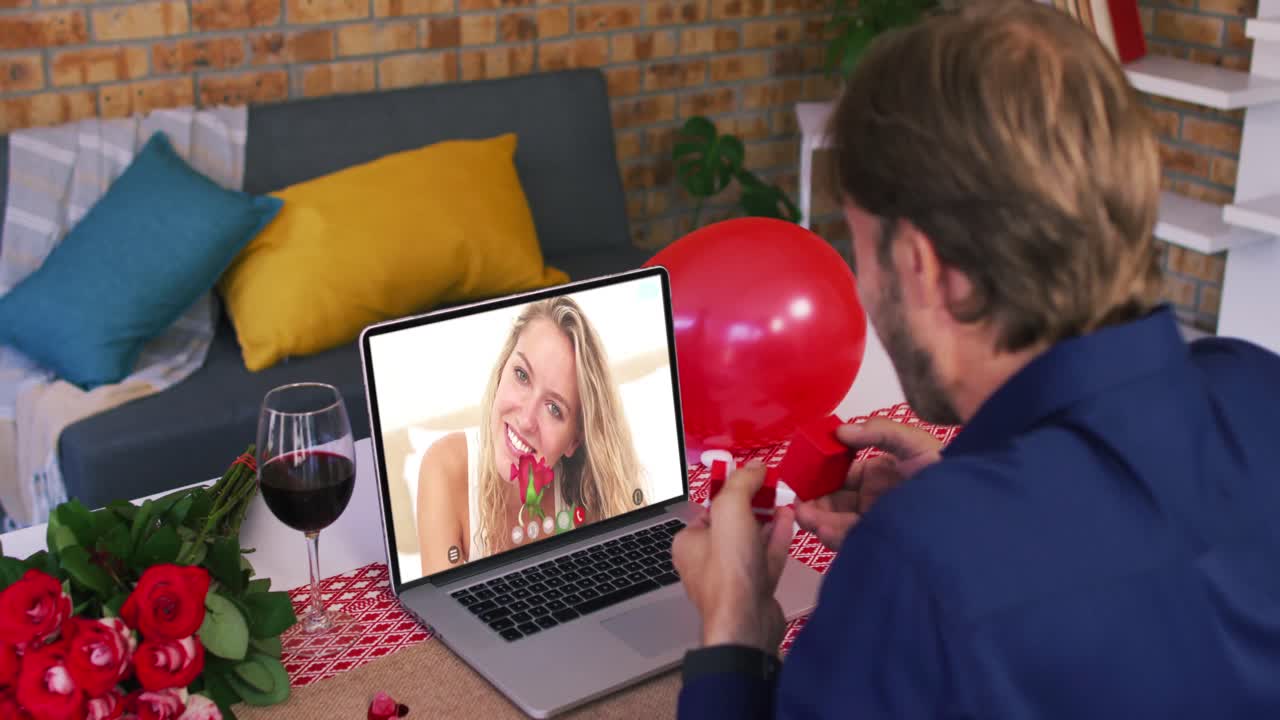 Coppia caucasica a un appuntamento di San Valentino in videochiamata, uomo che mostra un anello a una donna che tiene una rosa sullo schermo del portatile.
