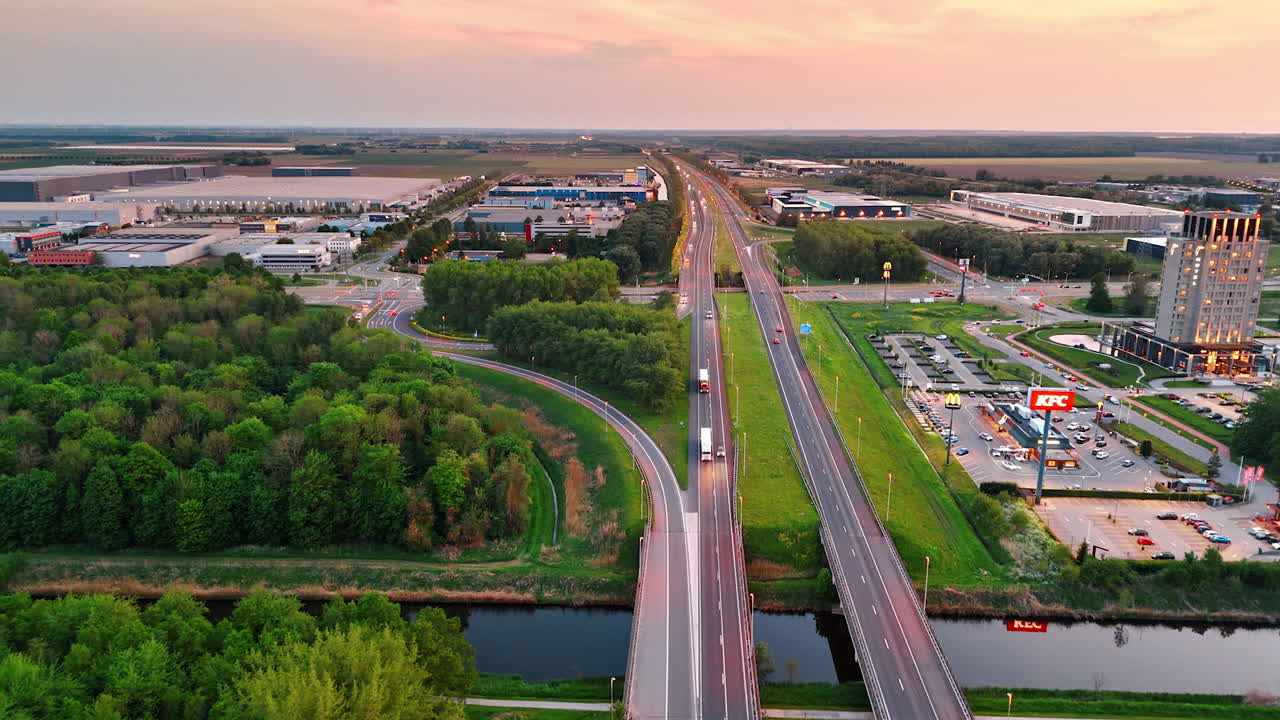 Flying over the highways crossing the countryside. Approaching parking lot and large storehouses. Aerial view.