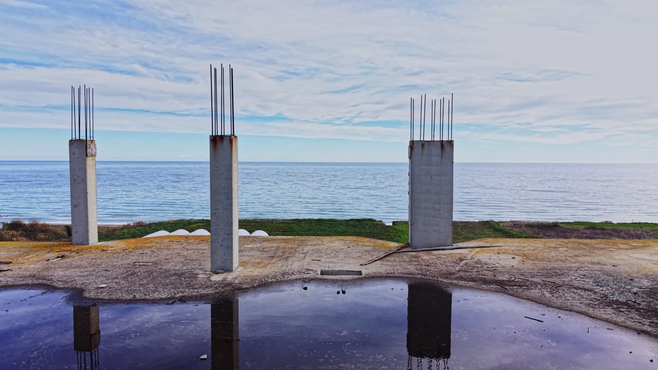 Construction site overlooking the ocean with concrete pillars and farmland