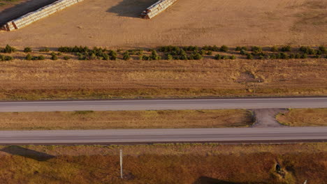 aerial view of a red pickup truck driving on a highway through rural farmland at sunrise or sunset.