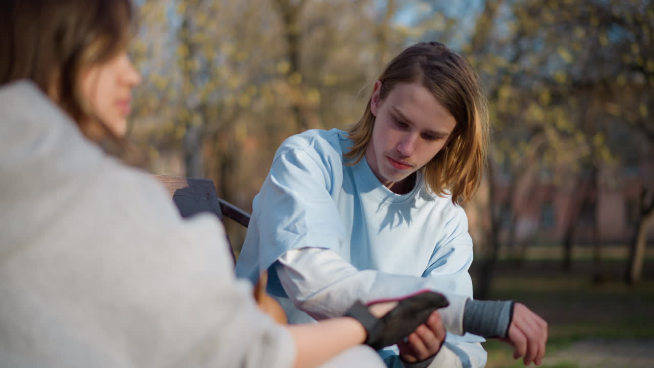 Протянутая рука помощи: человек оказывает практическую помощь другу под деревьями в лучах солнца — акт доброты, когда один помогает другому, поправляя браслет на запястье на открытом воздухе в теплых солнечных лучах.