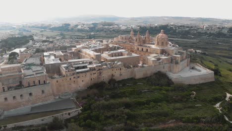 View-of-Mdina-city-outside-city-walls,-revealing-the-Cathedral-of-Saint-Paul---Aerial-Pan-forward-shot