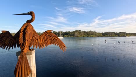 statue of a bird with wings spread by a lake