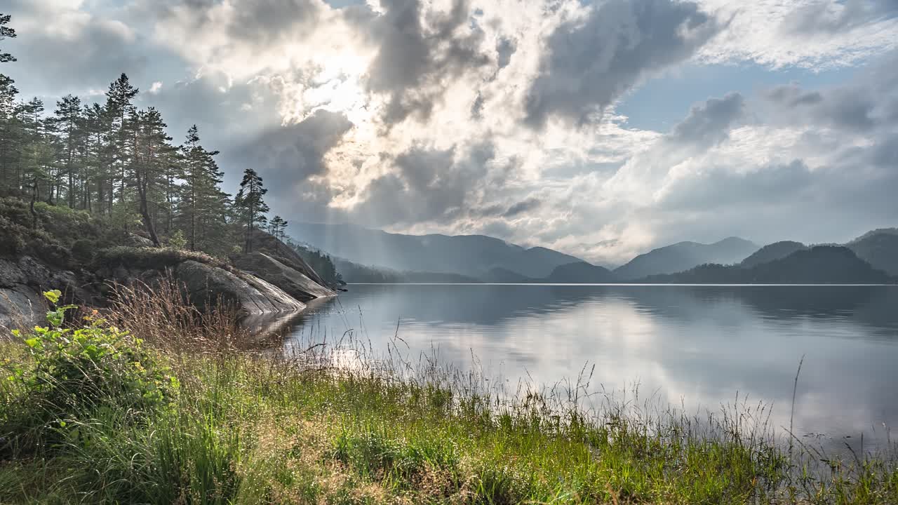los rayos del sol atraviesan las nubes tormentosas que giran sobre el lago y un bosque en un video timelapse