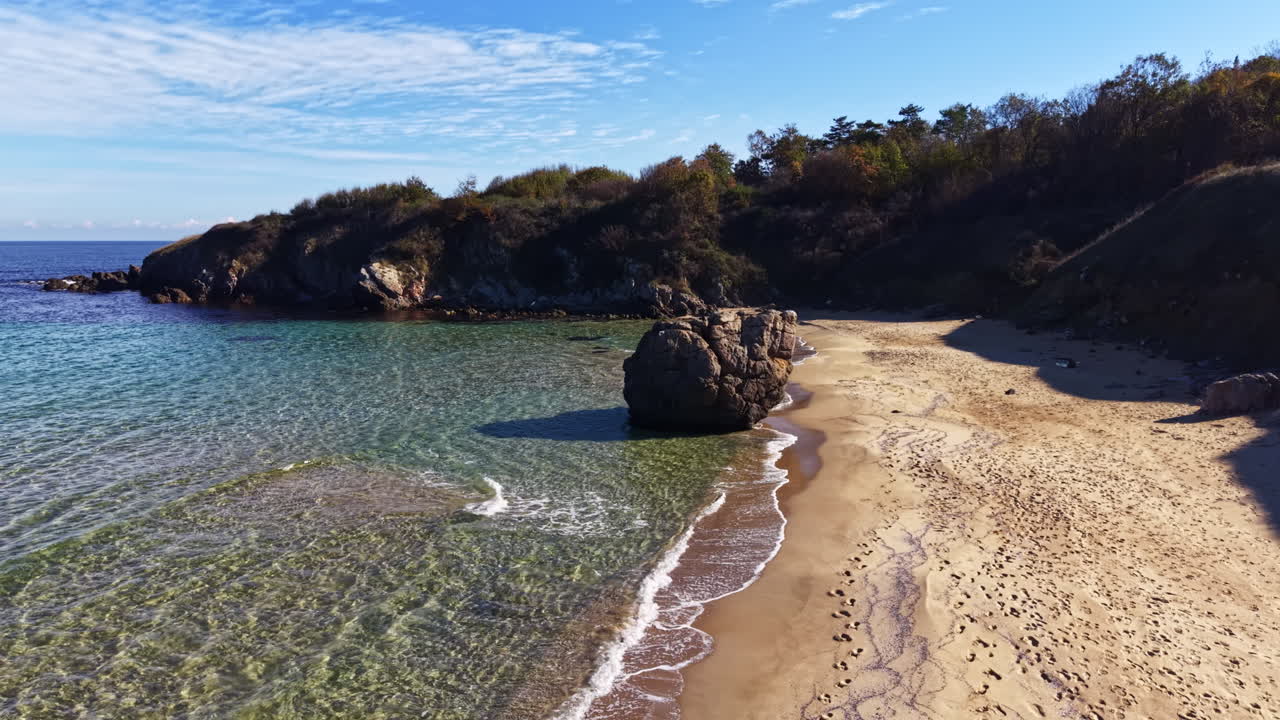 Spiaggia serena con affioramento roccioso e onde delicate sotto un cielo azzurro limpido nel tardo autunno