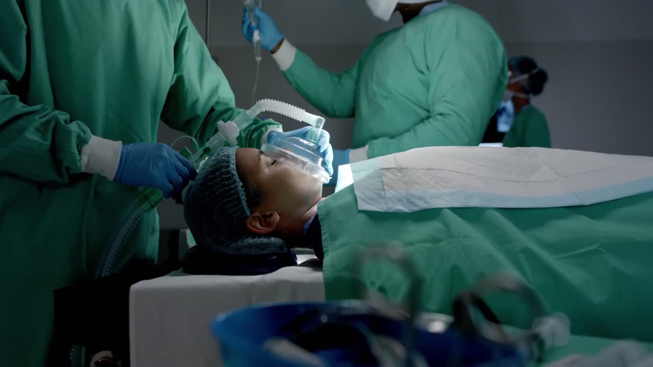 Chirurghi diversi con mascherine chirurgiche che applicano una maschera d'ossigeno a un paziente in sala operatoria al rallentatore