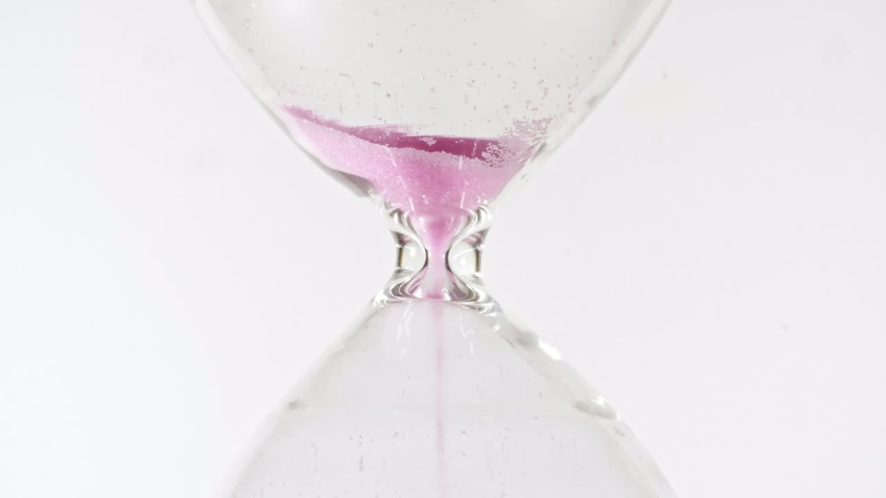 Hourglass on white isolated background. Pink sands move through hour glass. Macro shot.