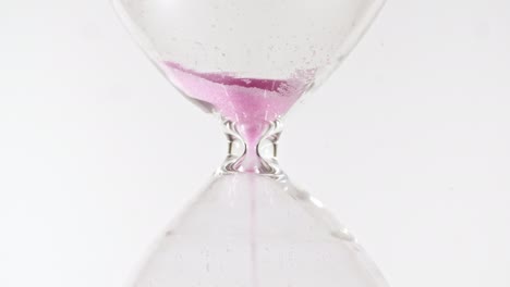 hourglass on white isolated background. pink sands move through hour glass. macro shot.