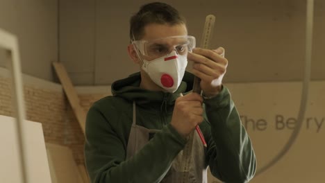 hardworking professional carpenter in mask and glasses holding a ruler and pencil