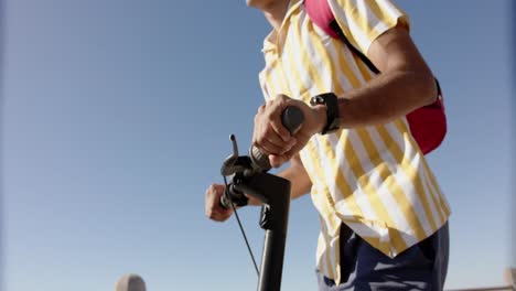 Happy-biracial-man-using-scooter-at-promenade-by-the-sea,-slow-motion