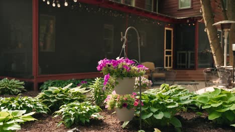 orbiting shot of a hanging flower pot gracefully suspended above the vibrant garden of flowers and shrubs