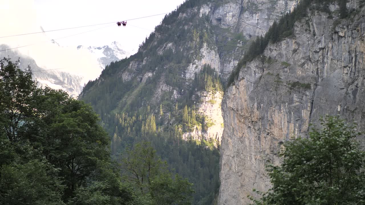 Slowly trees moving in the wind blowing true the valley with the sun and shadows reflecting on the mountains. Wide shot
