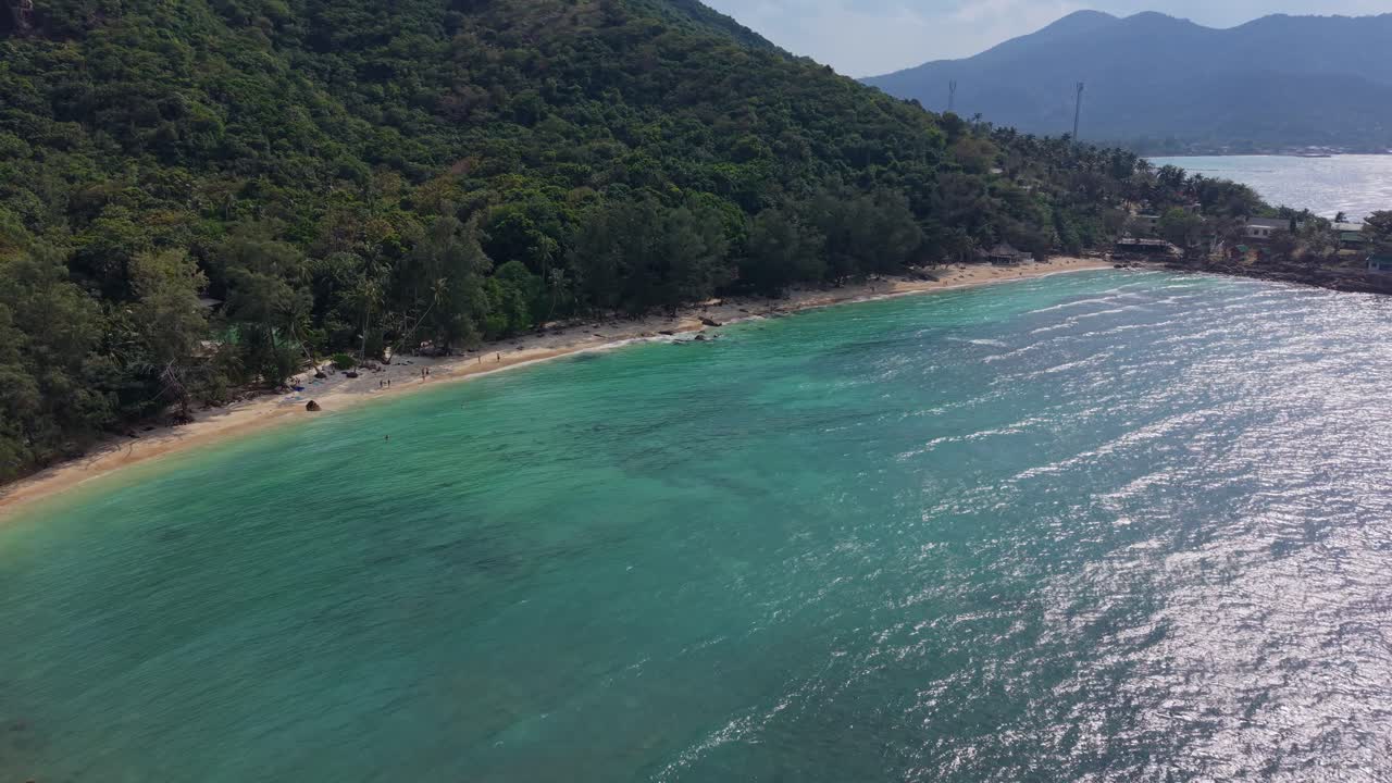 Lateral drone shot of a secluded beach cove with turquoise water and forested hills in Koh Samui, Thailand
