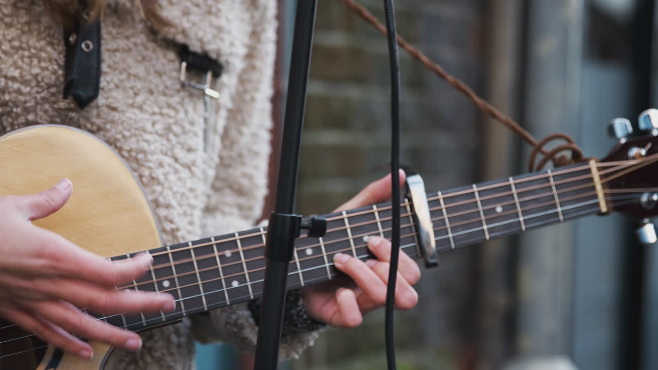 close up de una músico femenina tocando la guitarra acústica al aire libre en la calle