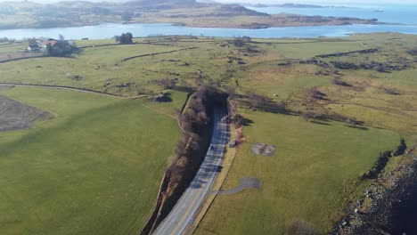 Subsea-byfjord-tunnel-in-Stavanger-Norway---Aerial-approaching-and-decending-towards-entrance-in-sunny-weather-and-surrounded-by-green-grasslands