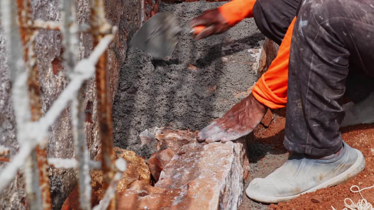 Lavoratore che versa malta cementizia su pietre di granito e livella per lavori di fondazione in cantiere. Di giorno, ripresa stabile, 4k.