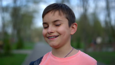 niño adolescente alegre mirando la cámara en el parque. tipo riendo en paréntesis posando al aire libre