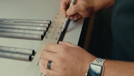 las manos masculinas usan una regla y un bolígrafo para medir la longitud del eje del palo de golf para un ajuste personalizado en el mostrador del taller en cámara lenta