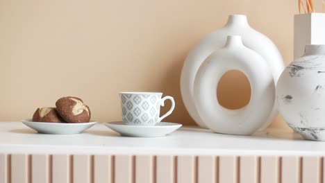 a cup of coffee and cookies on a white table with white vases