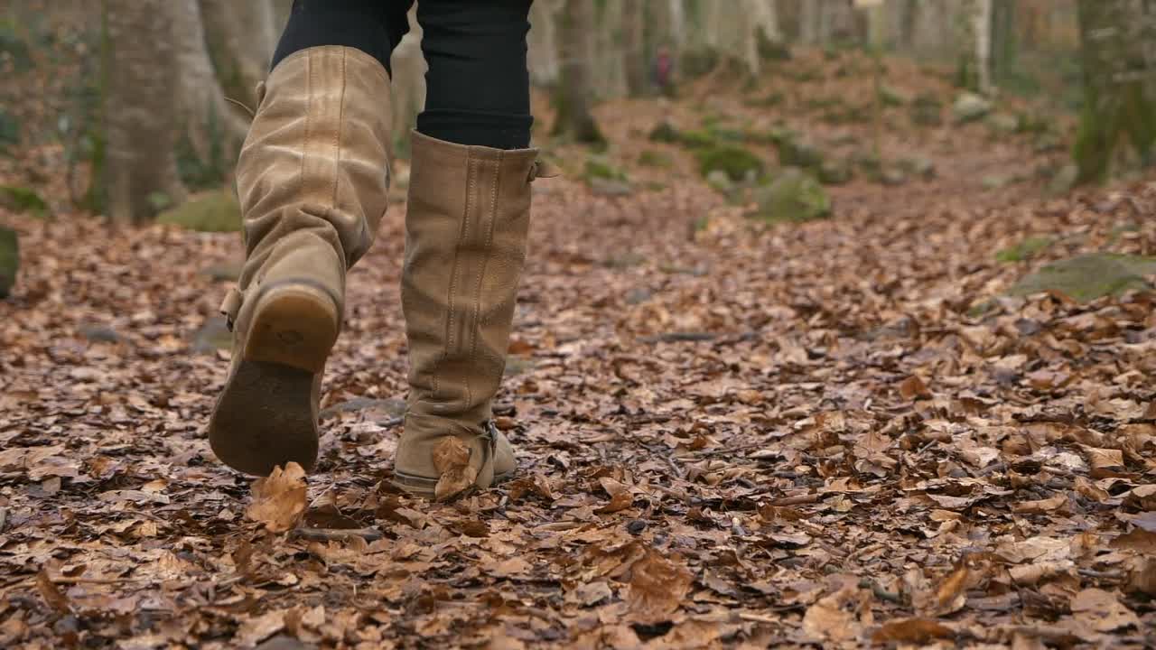 mujer con botas marrones altas caminando sobre hojas en el bosque de otoño, cámara lenta cerrada