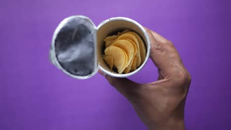 hand holding an open container of potato chips