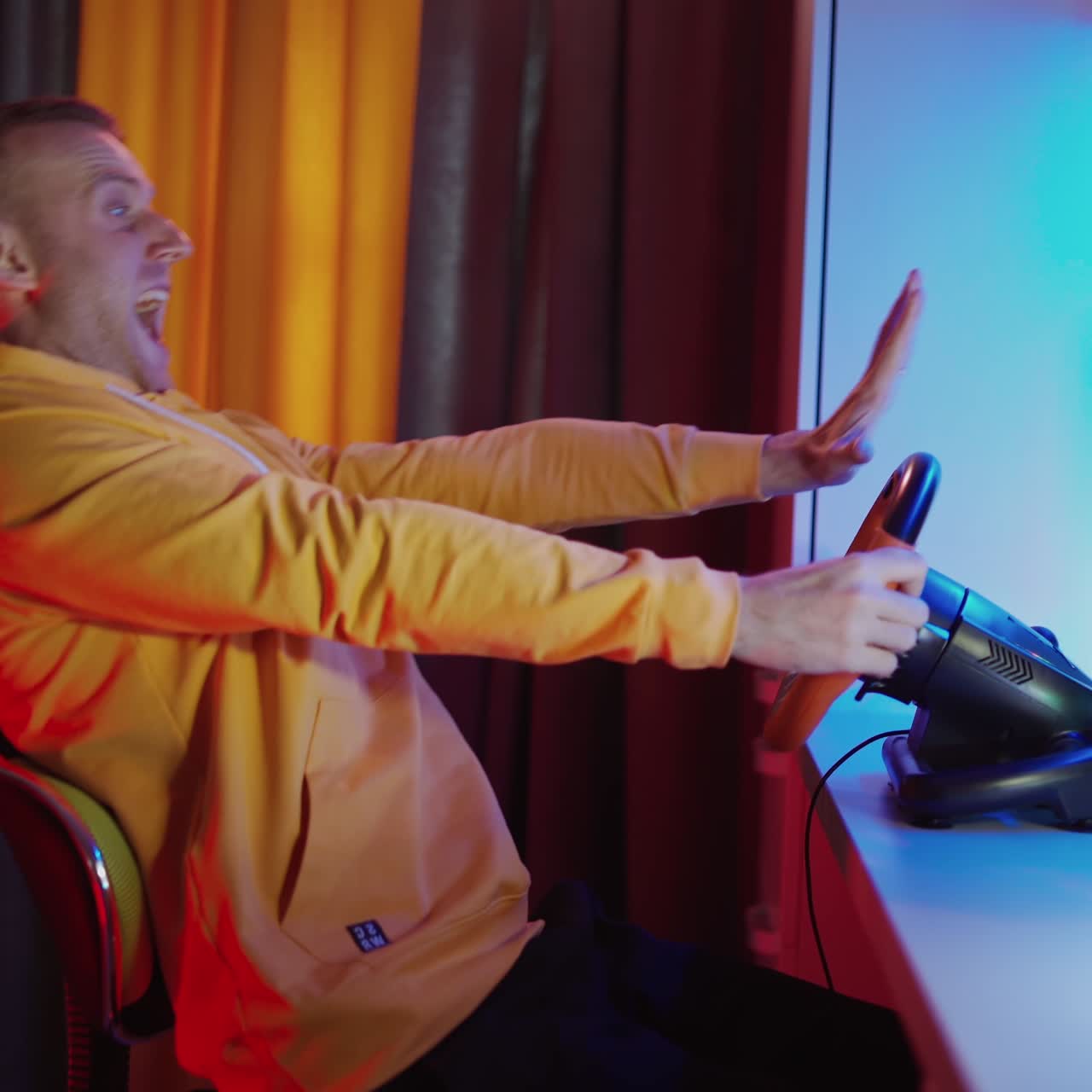 Happy man manages steering wheel in front of computer. Side view of a young man playing video games at home. Modern technology. Leisure time concept