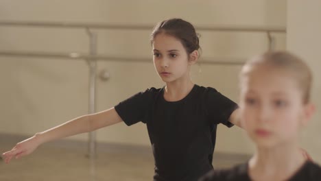 a group of young ballet students in black dancewear practicing positions in a spacious ballet studio with wooden flooring and wall-mounted barres. focused expressions and synchronized movements.