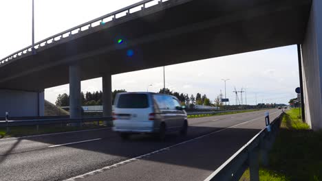 a bridge, overpass or an underpass going over pärnu highway during summer time while sun is shining and sky is slightly cloudy. cars and vehicles drive on the asphalt road that has markings on it.
