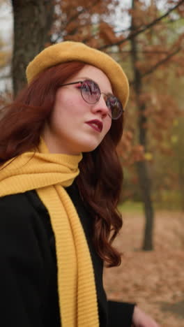 elegante dama con boina amarilla y silenciador a juego ajusta su cabello mientras camina a través de un parque de otoño, mostrando estilo y gracia en medio de vibrantes colores de otoño