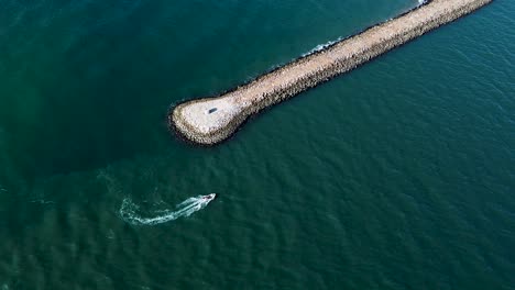 Small-ship-cruising-around-the-end-of-a-stone-jetty-in-the-atlantic-sea-on-the-shore-of-the-south-of-Portugal