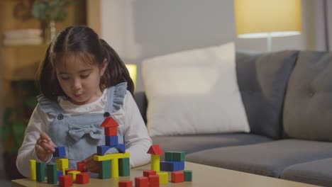 young girl at home playing with colourful wooden building blocks 3