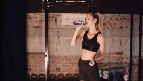 young female athlete drinking water from bottle after workout session at health club 2