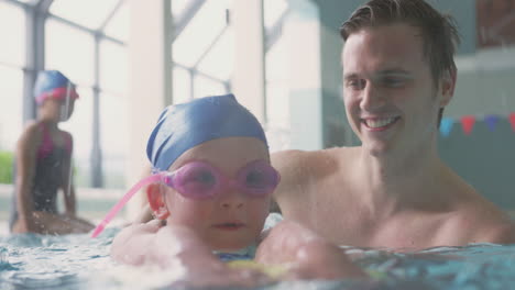 Männlicher-Schwimmtrainer-Gibt-Mädchen,-Das-Schwimmunterricht-Im-Pool-Hält