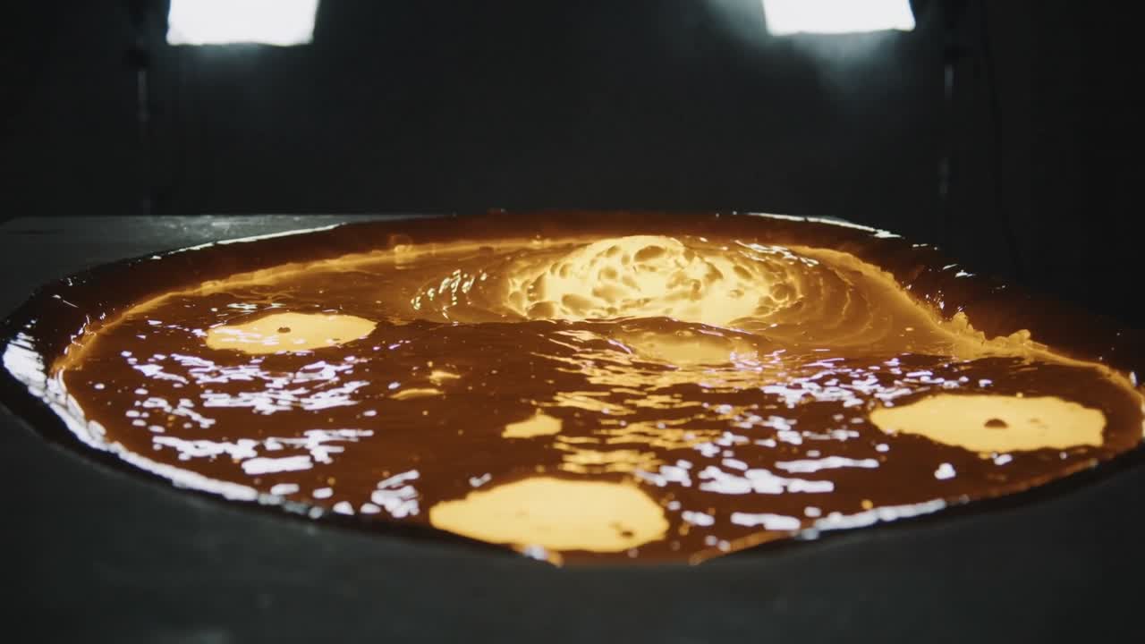 Pozza di metallo fuso in una fonderia industriale che sviluppa una cupola centrale dopo la formazione di un punto caldo, creando increspature.