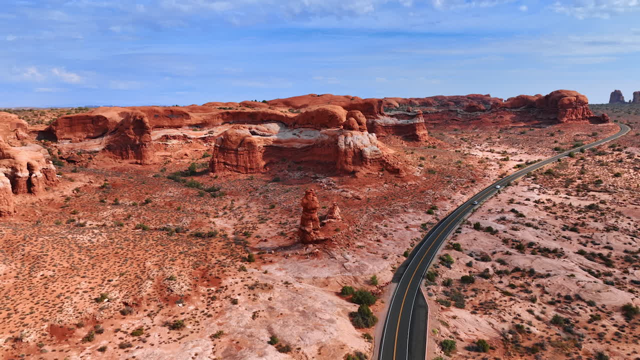 Following two cars moving by the highway in the desert. Approaching columns and walls of rocks in the Arches National Park, Utah, USA