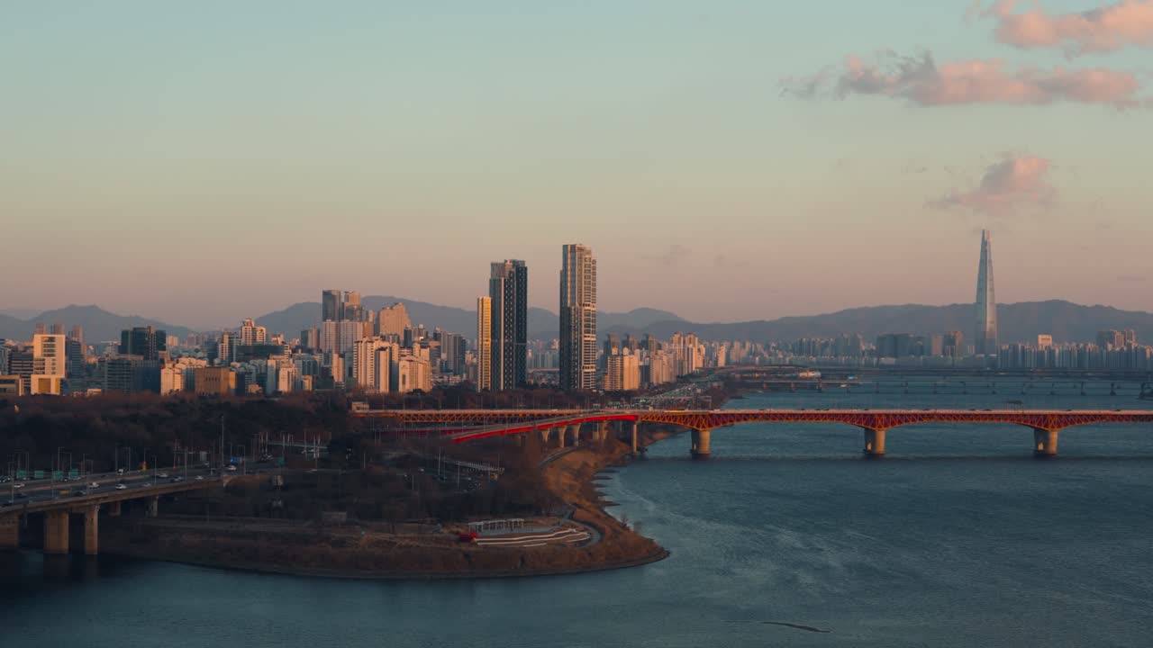 Ripresa aerea con drone del ponte Seongsu color arancio rossastro che attraversa il fiume Han, con l'autostrada Gangbyeonbuk-ro e il punto di riferimento Lotte World Tower sotto la calda luce del tramonto invernale a Seoul, Corea del Sud.