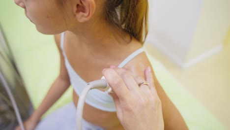 ultrasound scanning of child's shoulder joint. side view of a little girl during sonography procedure in clinic. doctor runs ultrasonic sensor over kid's arm.