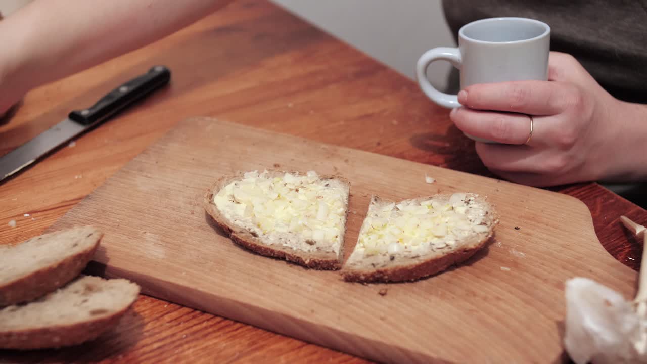 Woman's hands take a crystal glass with vodka, a cut slice of bread smeared with butter and garlic lies on a chopping board