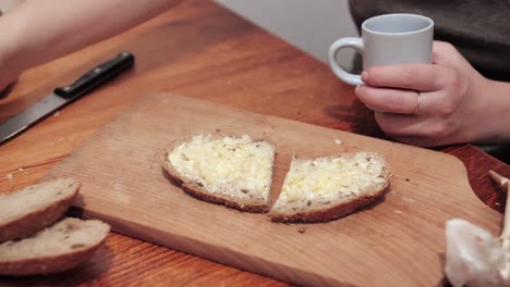 las manos de la mujer toman un vaso de cristal con vodka, una rebanada de pan untada con mantequilla y ajo se encuentra en una tabla de cortar