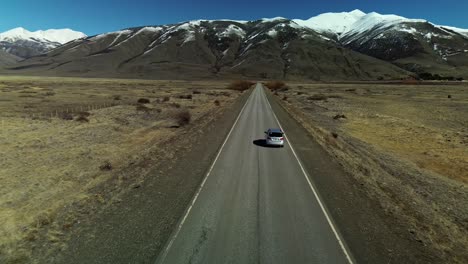 Vuelo-Hacia-Adelante-Con-Drones-Siguiendo-Un-Auto-Plateado-En-Una-Carretera-Escénica-Hacia-Las-Montañas-Patagónicas-Durante-El-Día-De-Verano,-Argentina