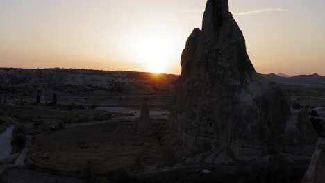 flying drone down next to fairy chimney rock formation as sun sets behind mountain in golden hour cappadocia turkey