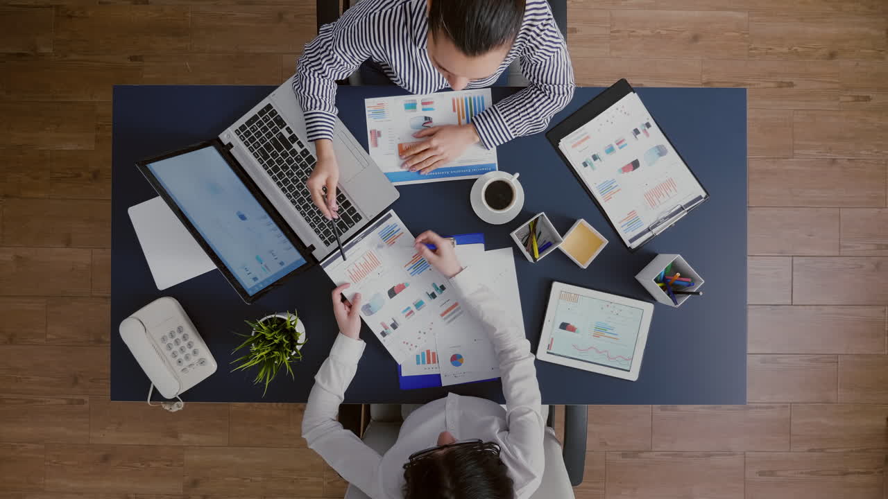 Top view of businesswomen shaking hands before analyzing management statistics paperwork