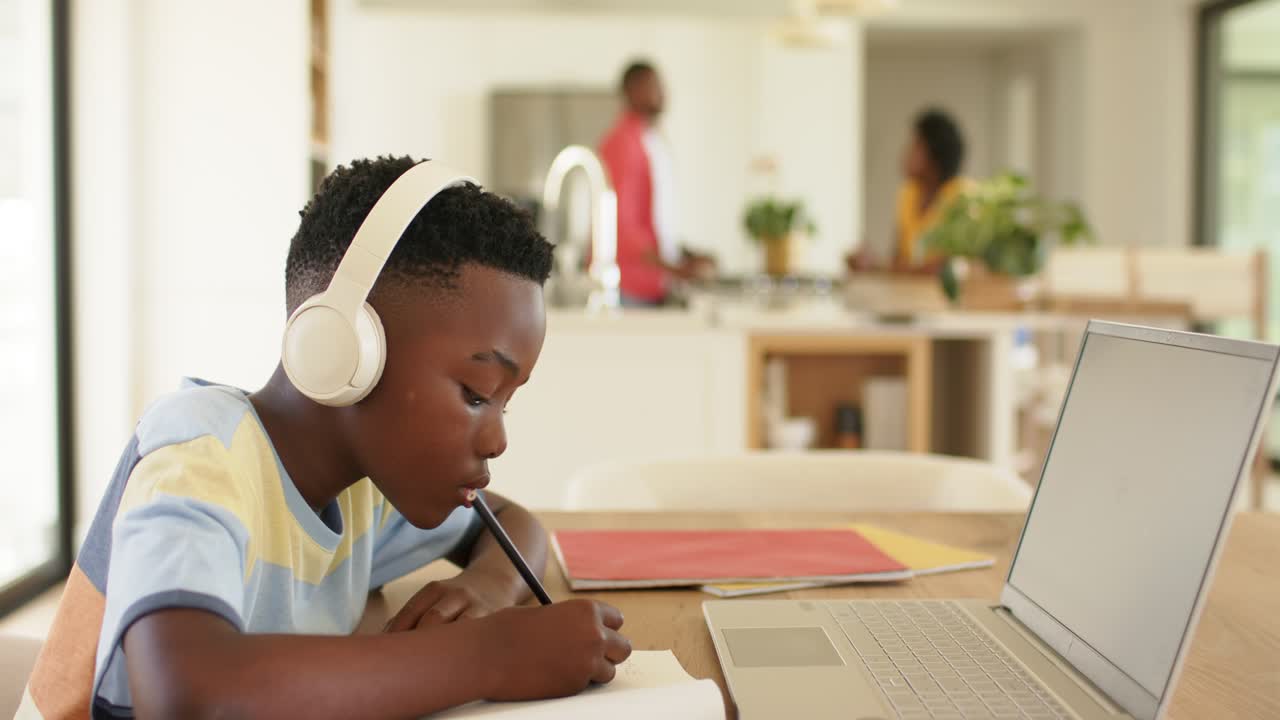 Homework driving African American boy wearing headphones taking notes on laptop at desk, copy space