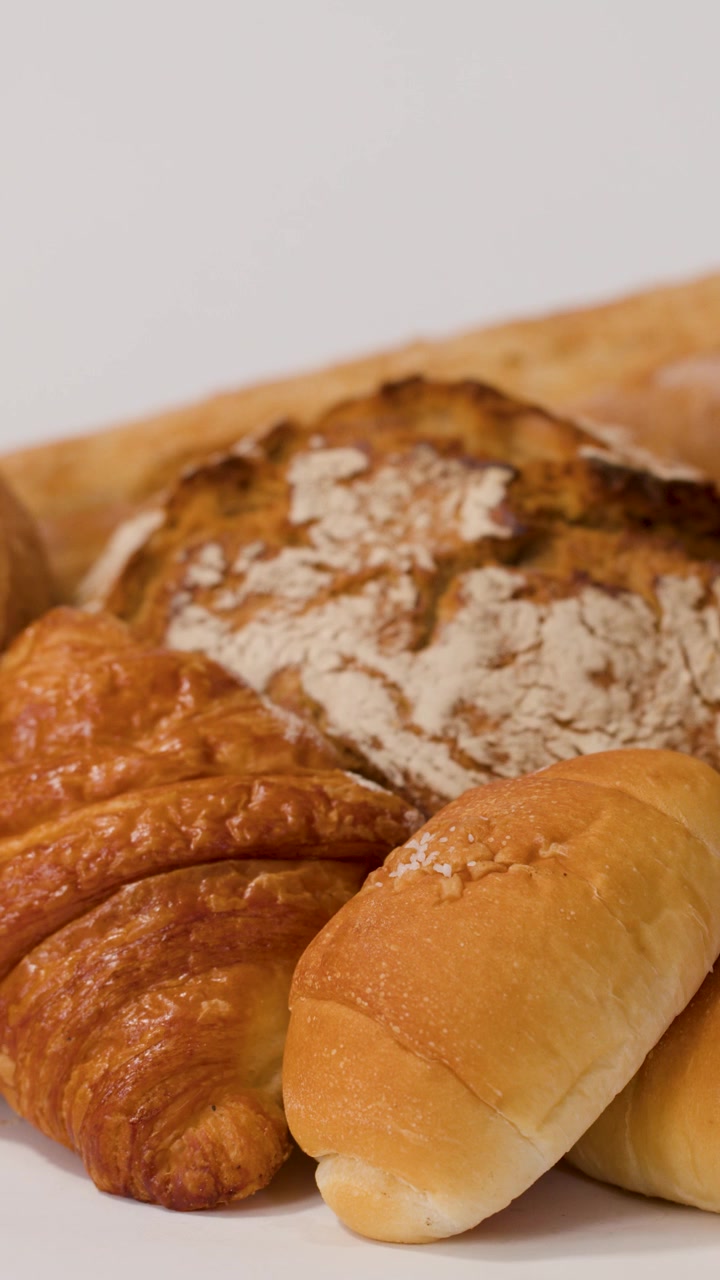 A hand places sliced multigrain bread onto a white surface with croissants and baguettes.