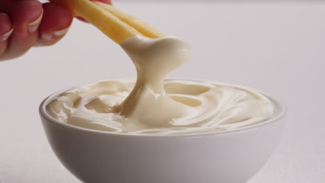 hand dipping french fries in mayonnaise