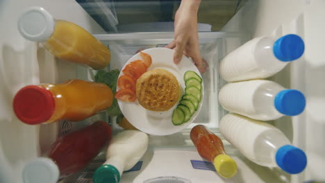 a man's hand takes a burger and a sauce from the refrigerator