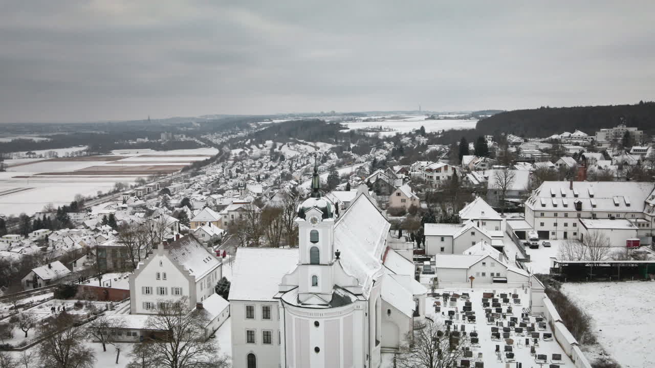 En 4K-drone sænkes ned over en snedækket kirke og landsbyens hustage. Et jævnt, lodret fald afslører en charmerende vinterstemning – ideel til reklamer, dokumentarfilm og visuelle elementer om turisme.