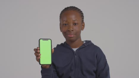 Studio-Portrait-Of-Boy-Holding-Green-Screen-Mobile-Phone-Against-Grey-Background